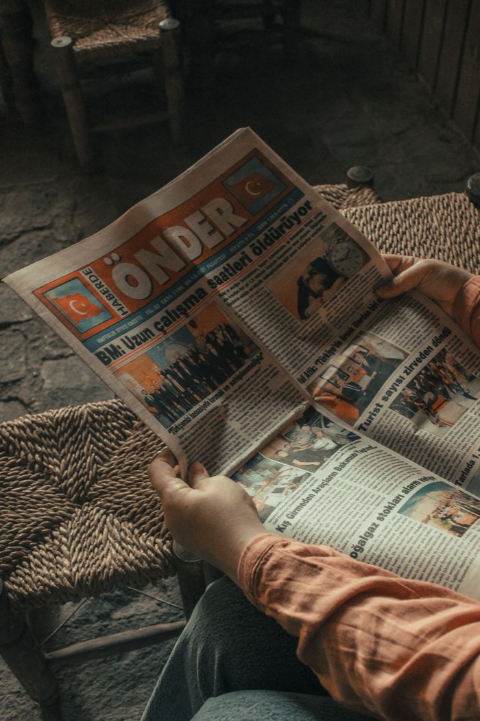 Close-up of person holding Turkish newspaper indoors on woven chair, creating a warm, vintage atmosphere.