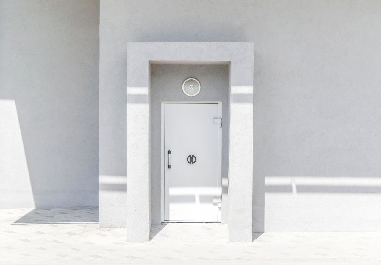 Services-02 A minimalist white door set against a plain wall, casting geometric shadows in natural sunlight.