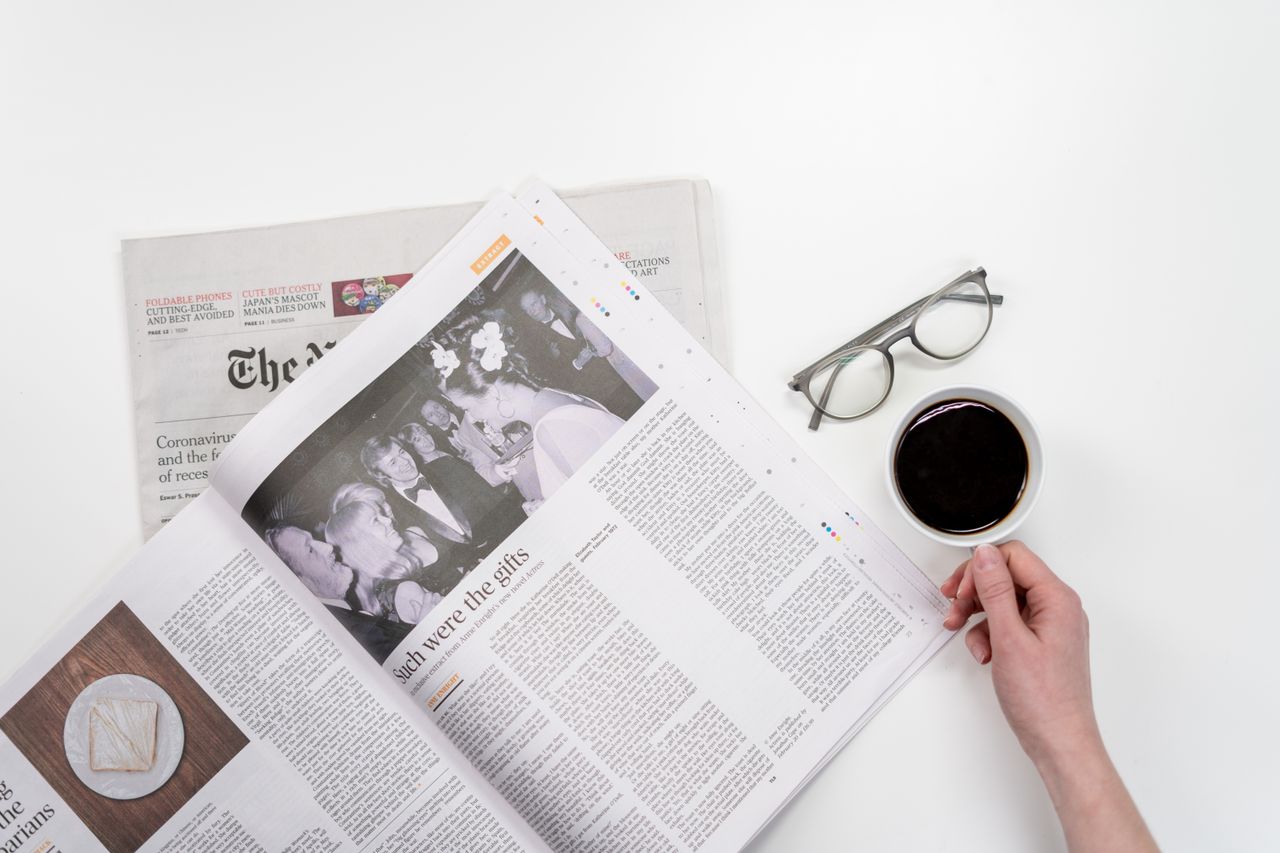 creative Overhead view of newspaper reading with coffee and glasses on a white table.